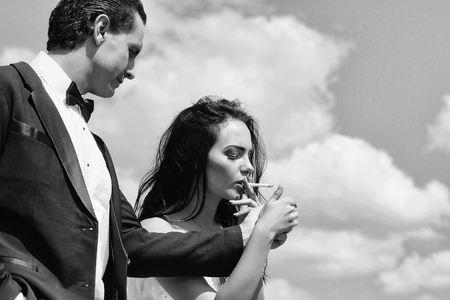 Elegant man offers to woman beautiful brunette gas lighter to light cigarette for smoking on blue skyの写真素材
