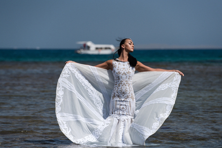Girl bride posing in wedding dress with white ship in sea water on sunny summer day on blue sky. Honeymoon travel conceptの写真素材