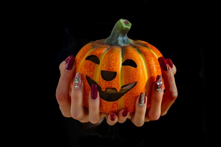 Halloween jack o lantern in female hands isolated on black background. Pumpkin and manicure with gems and sequins. Nail art concept. Holiday and party celebration. Autumn and harvest season.の写真素材