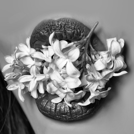 Sexy open female mouth of beautiful young woman with bright pink lips holds lilac flowers on face backgroundの写真素材