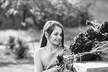 Pretty little girl in pink dress with smiling face standing near floral decoration of red roses sunny day outdoorの写真素材