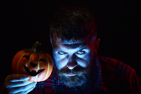 Halloween hipster with light on bearded face in dark. Man holding pumpkin. Magic illumination and jack o lantern. Autumn holiday celebration. Horror, mystery and evil concept.の写真素材