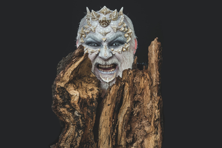 man or angry monster with thorns on face with futuristic makeup as alien with beard and lens in eyes...