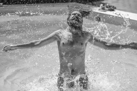 Young man hipster with smiling bearded face wet hair and body splashing water and having fun in...