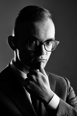 young fashion businessman with nerd glasses on thoughtful face and stylish hairdo in jacket with tie on studio backgroundの写真素材