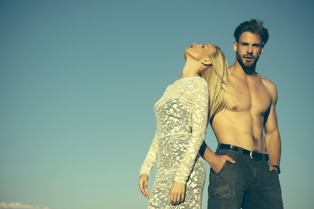 Woman or girl with long blond hair in lace dress. Man or macho with naked torso in jeans. Couple in love on blue sky. Fashion and beauty. Relationship, heterosexual and lifestyle concept, copy spaceの写真素材