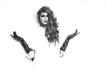 Pretty woman with long lush curly hair with hands in black leather gloves in torn paper isolated on white backgroundの写真素材