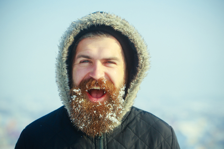 Christmas man with long beard. New year guy on blue sky with snow. Winter holiday and vacation. Xmas party celebration. Hipster in coat and hood.の写真素材