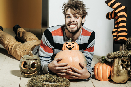 Halloween pumpkins, striped stockings and wreath. Man with messy hair happy smiling on floor. Autumn and harvest season. Holidays celebration concept. Trick or treat.の写真素材
