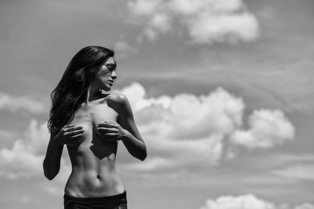Pretty girl young woman or girl model with slim sexy body and long brunette hair with bare chest or breast poses summer day on blue sky, copy spaceの写真素材