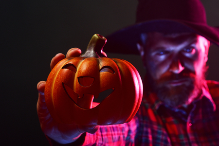 Halloween jack o lantern and blurred man. Mystery and magic concept. Autumn holiday celebration. Pumpkin in hand of hipster in wizard hat on dark background. Trick or treat.の写真素材