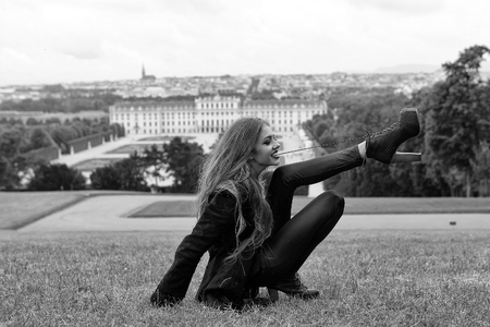 Young girl smiling with raised straight legs and long beautiful hair in fashionable clothes and boots on high heels with lace lying on green grass outdoorの写真素材