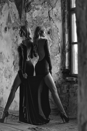 young pretty women with long lush curly blonde hair and thoughtful face in green dress standing near stony wallの写真素材