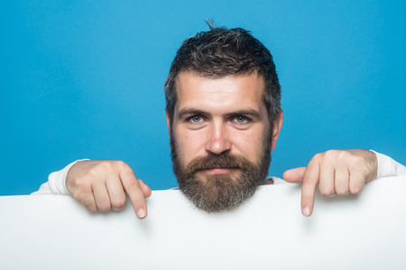 Hipster with happy face hold paper. Man with long beard and mustache. Feeling and emotions. Barber fashion and beauty marketing. Guy or bearded man on blue background.の写真素材
