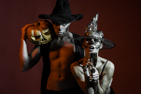 Halloween Couple in love with pumpkin and wine glass. Halloween Holiday and celebration. woman and man has happy face in witch hat. Zombie party and horror. couple with makeup on brown background.の写真素材