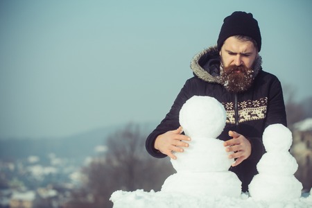 Winter holiday vacation and xmas party celebration. Snowman family made of white snow Christmas man with long beard. Santa claus hipster in coat and snowman. New year guy on blue sky with snow figure.の写真素材