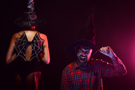 Halloween woman with bat wings on naked back. Man happy smiling on dark background. Couple in black witch hats. Costume party and holiday celebration. Trick or treat concept.の写真素材