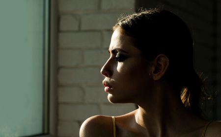 Girl or woman with face profile look at window on white brick wall. Contemplation, loneliness, solitude, depression concept.の写真素材