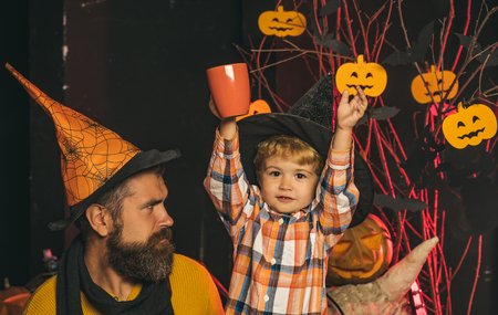 Halloween party and celebration. Halloween Holiday and celebration. man and child in witch hat. Father and small son drink from tea or milk cup. Boy kid with happy face and bearded man at pumpkin.の写真素材