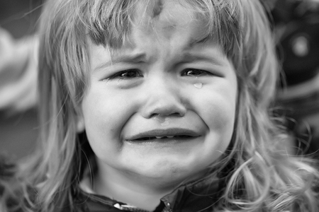 Little boy with cute emotional face and blond long hair cries with tears outdoorの写真素材