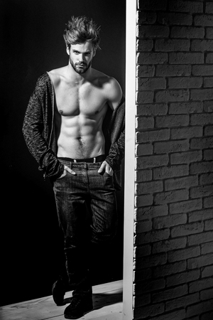 young handsome bearded sexy macho man with long beard and stylish hair in jacket and pants with muscular bare torso in studio on black and brick wall background, copy spaceの写真素材