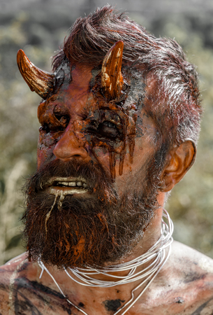 Halloween dragon creature on natural environment. Demon man with beard. Satan with red blood and wounds on face skin. Devil head with bloody horns. Temptation, hell, evil, horror, darkness concept.の写真素材