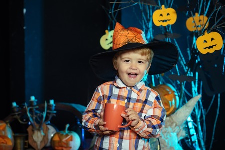 Halloween Holiday and celebration. Halloween child in witch hat. small boy drink from tea or milk cup. Boy kid with happy face at pumpkin. party and celebration.の写真素材