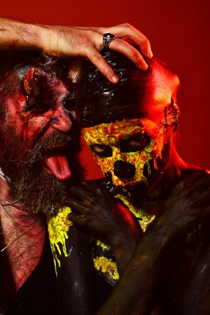 Halloween devil hipster with horns and girl skull makeup face. Trick or treat. Holiday, cosplay, celebration. Hell, death, life, evil concept. Man satan hold woman skeleton head on black background.の写真素材