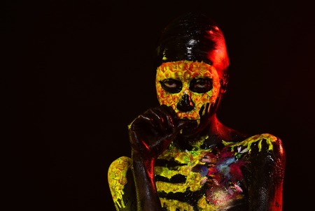 Halloween girl with skull face paint on black background. Woman skeleton with flower on chest. Day of dead celebration. Body painting and art. Life and death concept, copy spaceの写真素材
