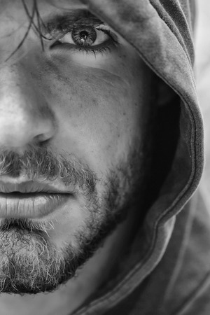 Bearded man young handsome guy male with beard and half face grey eye in hood on head outdoorsの写真素材
