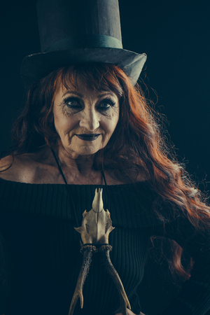 Halloween old lady in witch hat. Halloween old woman on black background. traditional party. holiday celebration. woman in black with long red hair and makeup.の写真素材
