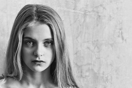 Pretty girl or cute young woman with blond hair and adorable face, has big blue eyes on textured wall background, copy spaceの写真素材