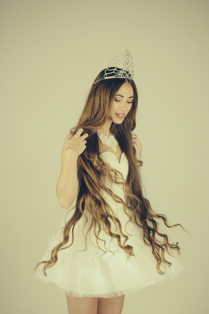 Beauty salon and wedding fashion. Girl has fashionable makeup and healthy hair on grey background. Woman with long hair white dress and crown. Haircare and prom queen. Hairdresser and cosmetics.の写真素材