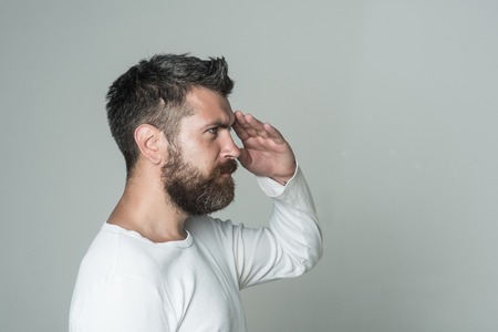 Barber fashion and beauty. Feeling and emotions. Guy or bearded man on grey background hold hand at head. Man with long beard and mustache. Hipster with serious face.の写真素材