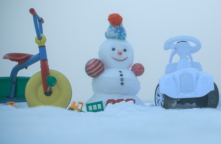 Tricycle, car and toys on snowy background. Christmas and new year. Holidays celebration concept. Festive surprise and presents. Snowman with smiley face on white sky.の写真素材