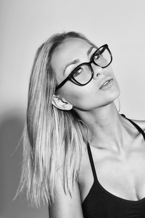 Pretty student girl or teacher woman in cute stylish eyeglasses with long blond hair wearing black bra, top on grey background. Education conceptの写真素材