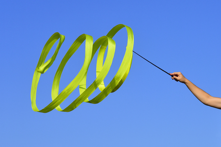 gymnastics green ribbon in hand of sport woman on blue sky backgroundの写真素材