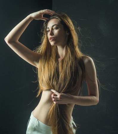 Girl has no makeup and healthy hair on black background. Beauty salon and fashion. Woman with stylish long hair and naked chest. Hairdresser and barber. Haircare and shampoo.の写真素材