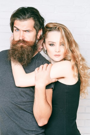 Couple in love hug on white brick wall. Girl and bearded hipster. Fashion, beauty, style concept. Man with beard and woman with long blond hair. Hipsterism, subculture, trend.の写真素材