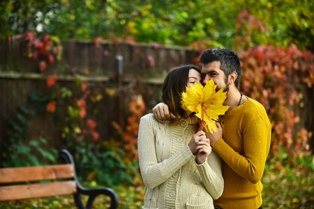 Man and woman with yellow tree leaves. Love relationship and romance. Nature season and fall holiday. Autumn happy couple of girl and man outdoor. Couple in love in autumn park at bench.の写真素材