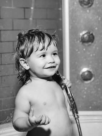 Cute happy smiling funny undressed boy child with blonde curly wet hair taking shower in bath with...
