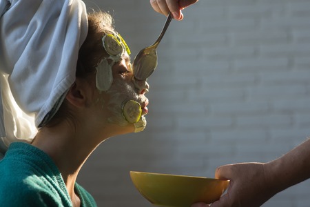Cosmetician hands with spoon and bowl. Girl or woman get cucumber mask on face. Skin care, spa, wellness. Rejuvenation, health, youth. Beauty salon concept.の写真素材