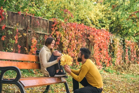 Autumn happy couple of girl and man outdoor. Love relationship and romance. Couple in love in autumn park at bench. Nature season and fall holiday. Man and woman with yellow tree leaves.の写真素材