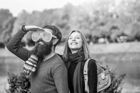 Young couple of pretty girl and bearded man hipster with funny orange eyeglasses outdoors in park on autumn day on natural backgroundの写真素材