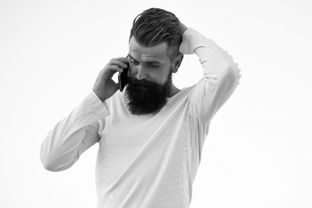 One handsome young bearded thoughtful business man in white sweater holding and speaking on cell phone outdoor on light sky natural background, horizontal pictureの写真素材