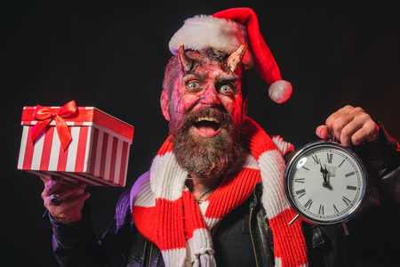 Halloween or christmas man devil hold present box and clock. Hipster smile with satan horns in santa...