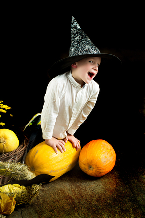 Halloween Kid with orange pumpkin in witch hat. Small boy in spider web hat. Halloween child with happy face. Party and traditional food. Holiday and celebration.の写真素材