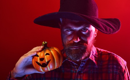 Halloween man with beard and jack o lantern. Hipster in wizard hat holding pumpkin on red background. Trick or treat. Autumn holiday celebration. Mystery and magic concept.の写真素材