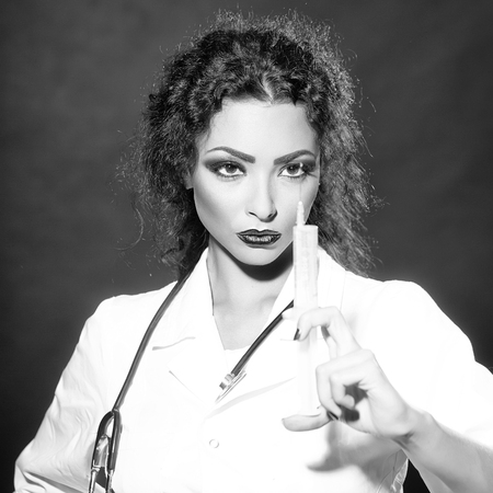 Closeup view portrait of one serious sexual beautiful brunette medical worker with stethoscope in white nurse uniform holding injecting suringe for botox shot or drugs in studio, square pictureの写真素材