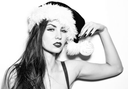 Pretty girl young beautiful cute woman sexy female model with long brunette hair in traditional santa claus new year red hat poses with Christmas bauble isolated on whiteの写真素材